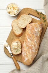 Cut baguette with butter and herbs on white wooden table, flat lay