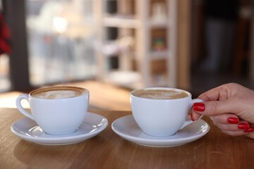 Woman having coffee break at wooden table with two cups in cafe, closeup