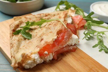 Delicious crepes with salmon, cream cheese and arugula on blue wooden table, closeup