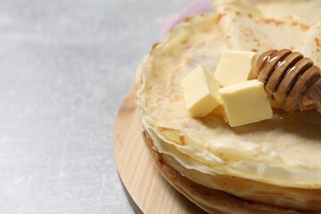 Tasty crepes with butter and honey on grey textured table, closeup. Space for text