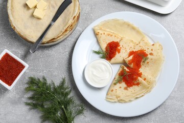 Tasty crepes with red caviar, dill and sauce served on grey textured table, flat lay