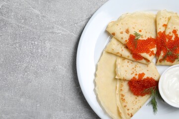 Tasty crepes with red caviar, dill and sauce on grey textured table, top view. Space for text