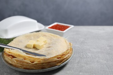 Stack of tasty crepes with butter on grey textured table, closeup. Space for text