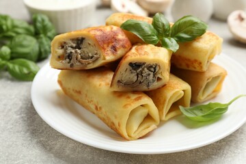 Delicious rolled crepes with mushrooms and basil on grey table, closeup