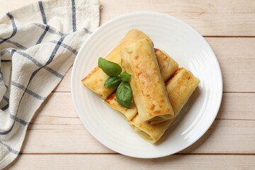 Delicious rolled crepes with basil on wooden table, top view