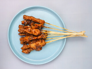 Juicy grilled chicken satay on a blue plate, ready to serve.