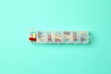 Plastic container with various pills on colored background