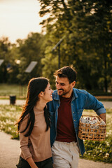 Happy couple walking together in a public park carrying a picnic basket