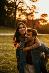 Happy couple having a piggyback ride in a beautiful park during sunset