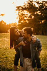 Fototapeta premium Happy couple having a piggyback ride in a beautiful park during sunset