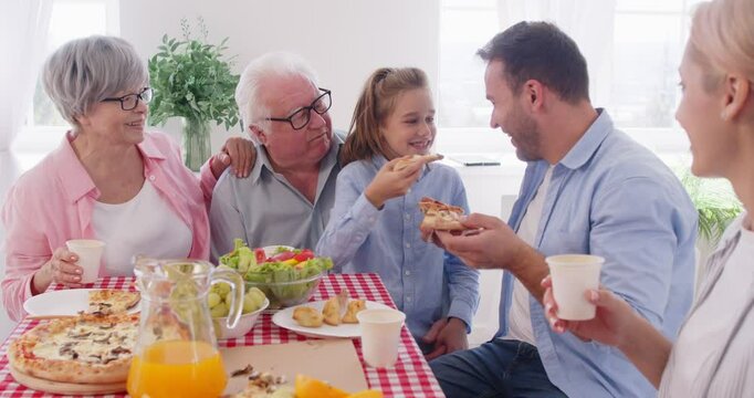 Happy family at table, smiling three generations eating together at home, enjoying meeting together having fun at party, eating delivery Italian fast food pizza, parents, grandparents, child weekend