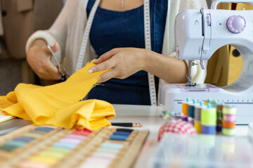 A woman who is running an online clothing business and is also a designer, working on designing clothes and preparing them to be packed in boxes to be delivered to customers.