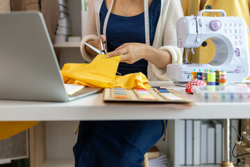 A woman who is running an online clothing business and is also a designer, working on designing clothes and preparing them to be packed in boxes to be delivered to customers.