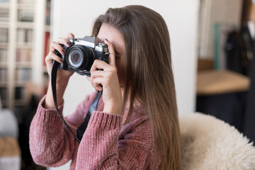 Young woman taking a photo with a vintage camera indoors.