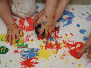 Mom plays with children, funny baby shows his palms painted with paint. Creative art classes. Laughter. Happy children and mom finger painting on paper at home. Bright colors, gouache and watercolors