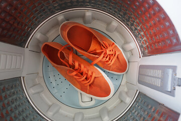 Two bright orange sneakers with shoelaces rest inside a washing machine after washing. 
