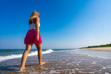 Naklejka premium Summer vacations. Beautiful mature woman walking on sandy beach on beautiful sunny day. Back view