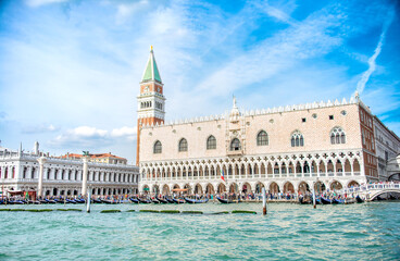 Fototapeta premium As seen from a ferry sailing on the Grand Canal, the Piazza San Marco, St. Marks Clocktower, Column of the Lion and the Gondoliers with their moored Gondolas on a summer day in Venice, Italy.