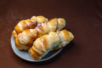 Freshly baked croissants with a golden crust and an appetizing appearance on a gray plate lying on a brown background.