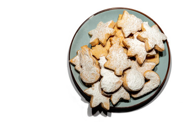 New Year's cookies of various shapes: Christmas trees, stars, snowmen, sticks on a blue plate, sprinkled with powdered sugar on a white background.
