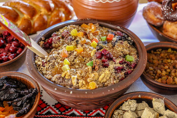 Traditional Ukrainian kutya with honey, nuts, dried fruits and poppy seeds in a clay bowl. Around the bowl are other festive dishes: loaf, dried fruits.