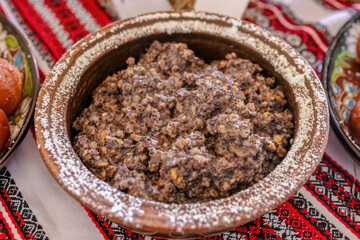 Traditional sweet ceremonial Ukrainian wheat kutya with honey, nuts, dried fruits, and poppy seeds is served in a clay bowl on a festive table covered with an embroidered tablecloth.