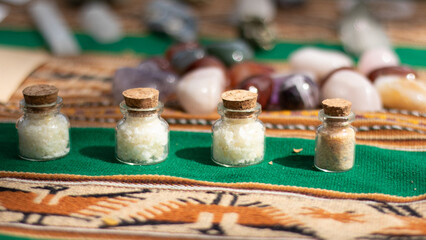 Small bottles filled with crushed quartz on a table and some colored quartz behind them