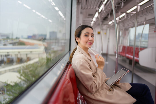 Young businesswoman is using her digital tablet while commuting to work by train, enjoying the convenience and productivity of modern technology during her daily commute