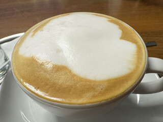 Creamy cappuccino coffee with foam in a white cup on a wooden table