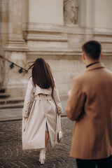 A girl in a beige long raincoat with a handbag walks away from the boy. Farewell. Separation.