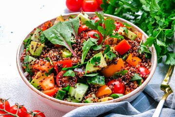 Quinoa salad with tomatoes, paprika, avocado, cucumbers and parsley. White table background, top view