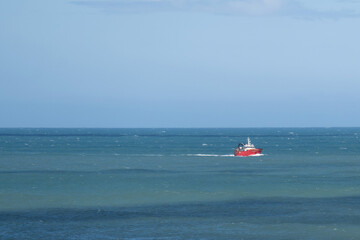 Red fishnig offshore vessel sailing across a calm ocean under a clear blue sky. Maritime industry themes, logistics, transportation, and oceanic exploration visuals