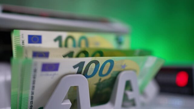 Cash machine switches on and blades start to rotate. Stack of one hundred euro banknotes appears. Close up.