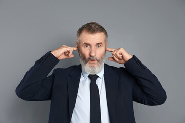 Senior man covering his ears with fingers on grey background