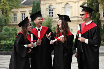 Happy students with diplomas after graduation ceremony outdoors