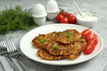 Delicious potato pancakes with fresh tomatoes served on grey table