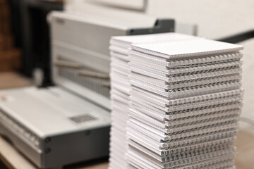 Modern binding machine and stacks of notebooks on table indoors, selective focus