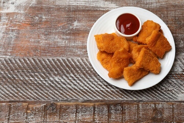 Delicious chicken nuggets with ketchup on wooden table, top view. Space for text