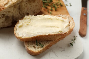 Fresh bread with butter and thyme on white table, closeup