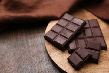 Pieces of delicious dark chocolate bar on wooden table, closeup. Space for text