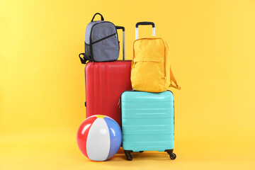 Travel abroad. Packed suitcases, beach ball and backpacks on yellow background
