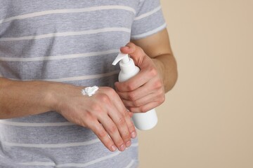 Man applying hand cream from pump bottle on beige background, closeup. Space for text