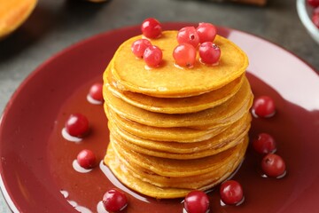 Tasty pumpkin pancakes with cranberries and honey on table, closeup