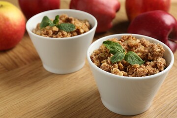 Delicious apple crisp with mint in bowls and fresh fruits on wooden table, closeup