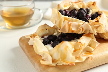 Delicious puff pastries with blueberries and tea on white table, closeup