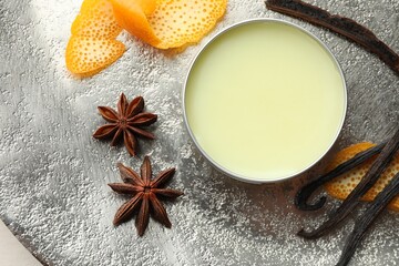 Natural solid perfume in container, vanilla pods, anise stars and orange peels on grey table, flat lay