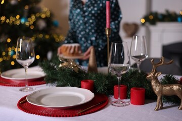 Woman setting table for Christmas dinner at home, focus on dishware, glasses and decor