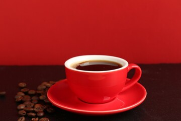 Red cup with coffee and roasted beans on black table