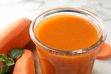 Fresh carrot juice in glass, vegetables and mint on light table, closeup