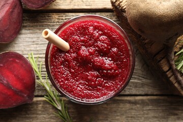 Fresh beetroot smoothie in glass, rosemary and cut vegetable on wooden table, flat lay
